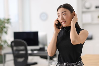 Portrait of beautiful businesswoman talking on smartphone in office. Space for text