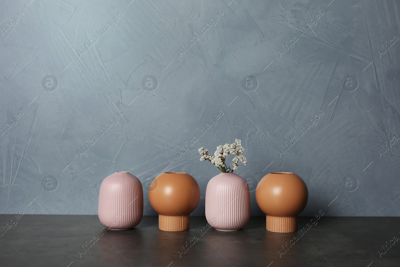 Photo of Beautiful ceramic vases and flowers on table against color wall. Space for text