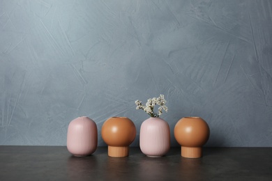 Photo of Beautiful ceramic vases and flowers on table against color wall. Space for text