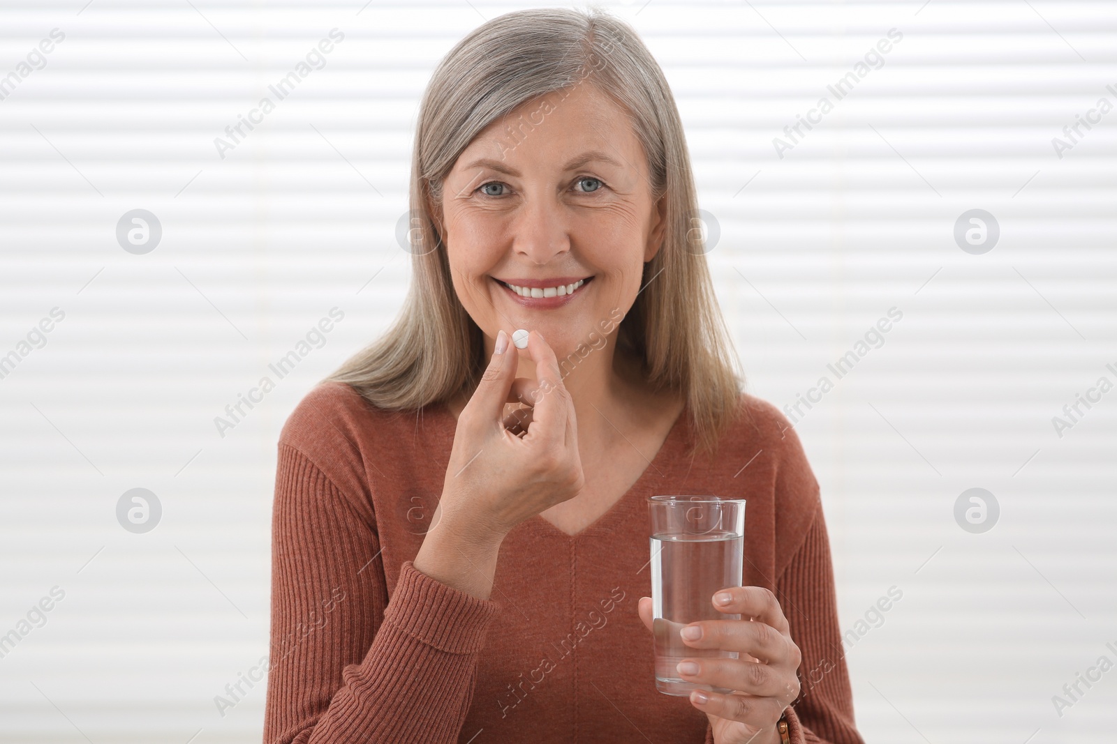 Photo of Senior woman with glass of water taking pill indoors