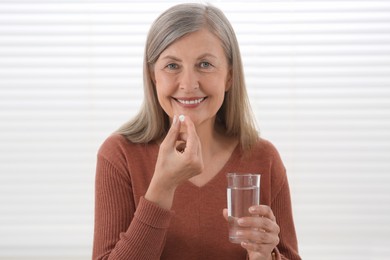 Senior woman with glass of water taking pill indoors