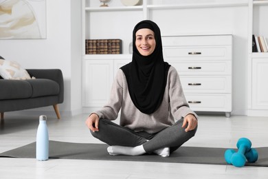 Photo of Muslim woman in hijab meditating on fitness mat at home