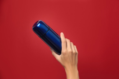 Photo of Woman holding modern blue thermos on red background, closeup