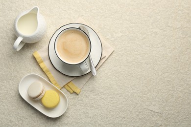 Photo of Tasty cappuccino in cup, milk and macarons on light textured table, flat lay. Space for text