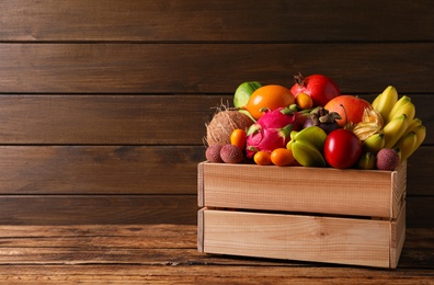 Crate with different exotic fruits on wooden table. Space for text