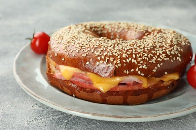 Delicious bagel with ham and cheese on light grey textured table, closeup