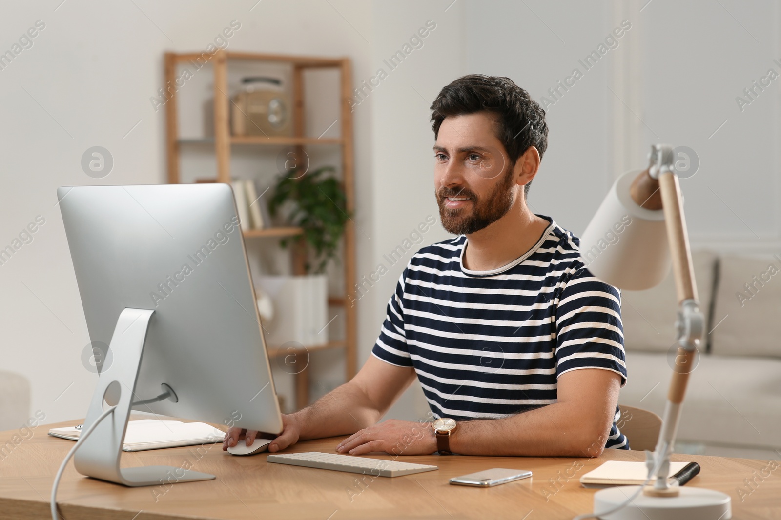 Photo of Home workplace. Happy man working with computer at wooden desk in room