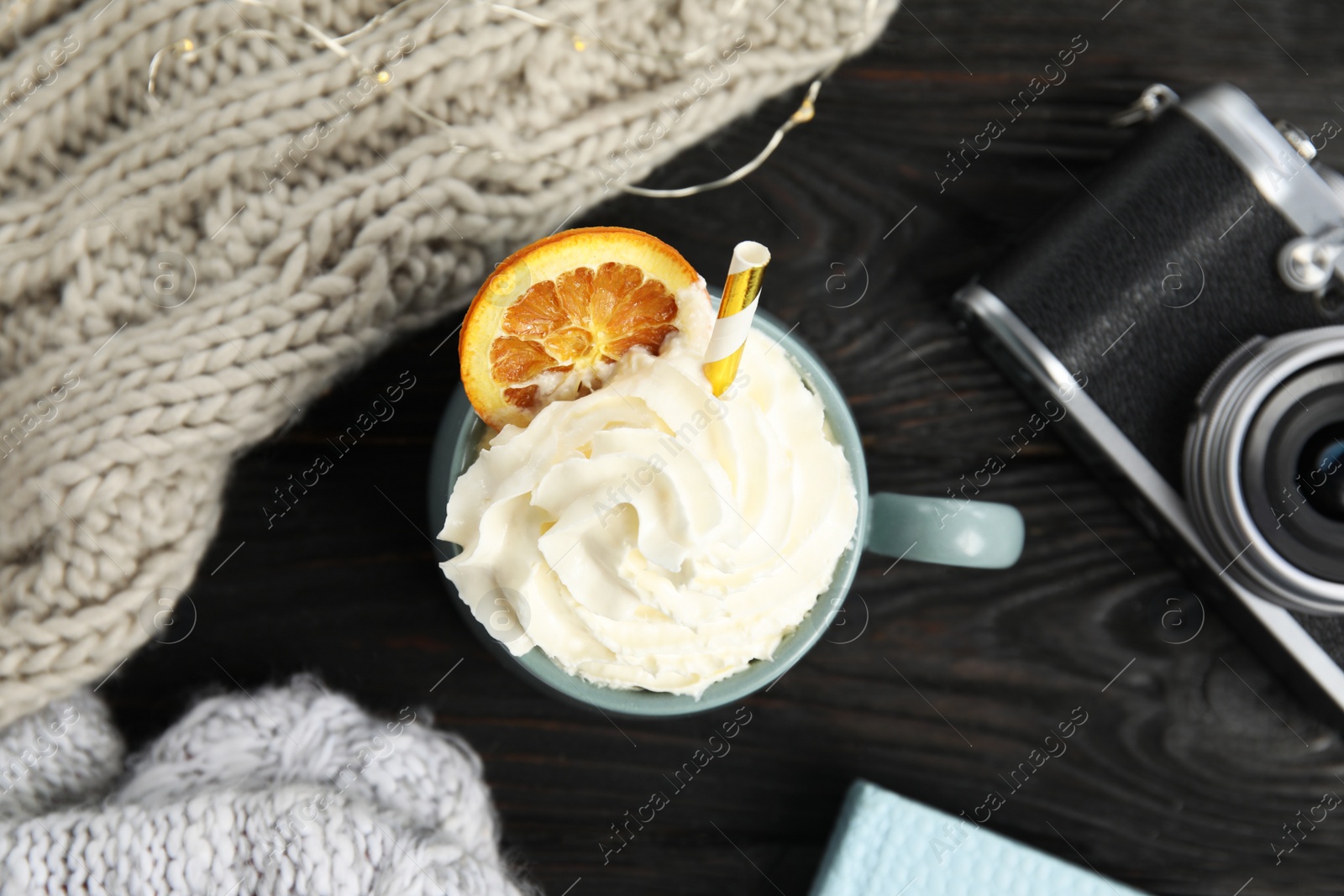 Photo of Cup of hot winter drink with whipped cream and knitted scarf on black wooden table