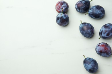 Tasty ripe plums on white marble table, flat lay. Space for text