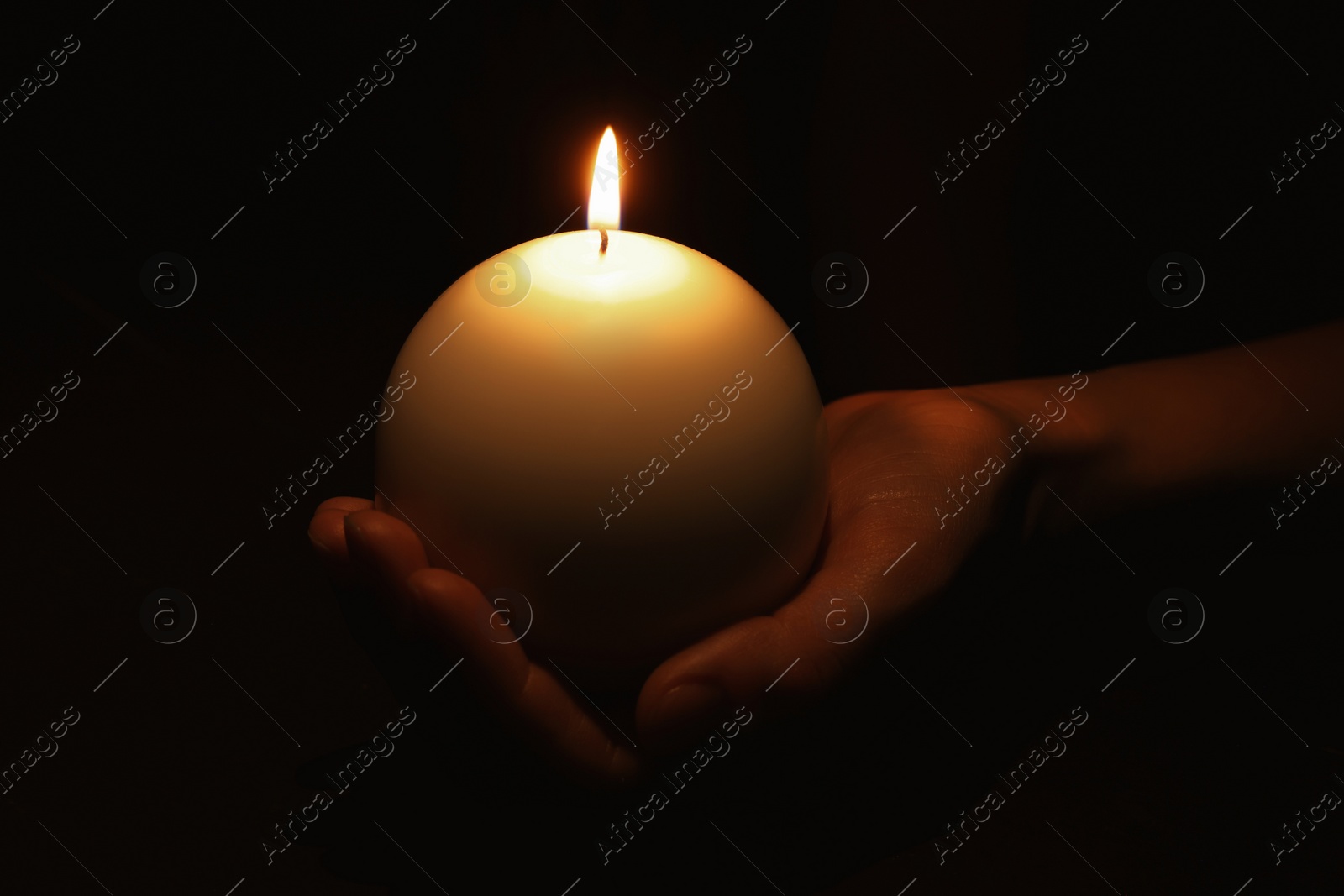 Photo of Woman holding burning candle in hand on black background, closeup