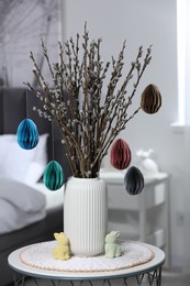 Photo of Beautiful pussy willow branches with paper eggs in vase and bunny figures on table at home. Easter decor