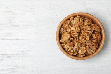 Tasty walnuts in bowl and space for text on wooden background, top view
