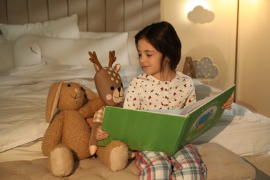 Photo of Little girl reading book in bedroom lit by night lamp
