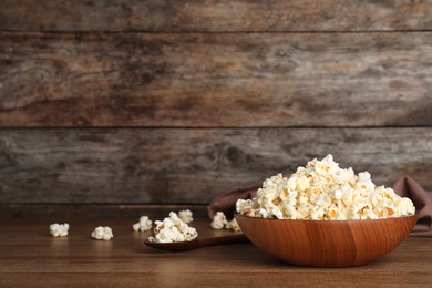 Photo of Wooden bowl with tasty popcorn on table. Space for text