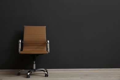 Photo of Comfortable office chair near black wall indoors. Space for text