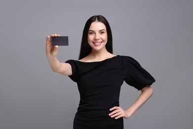 Happy woman holding blank business card on grey background