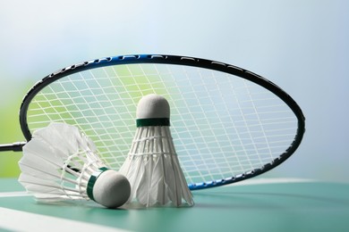 Photo of Feather badminton shuttlecocks and racket on green table against blurred background, closeup