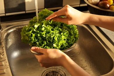 Photo of Woman washing fresh lettuce leaves in metal colander, closeup