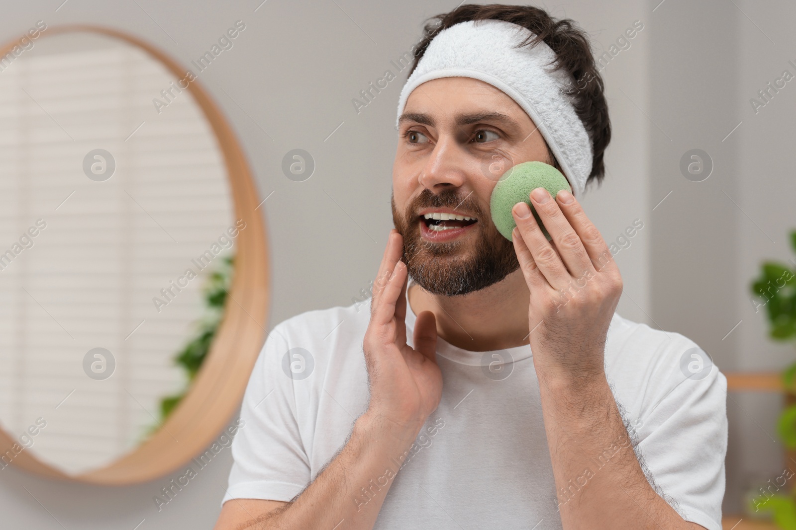 Photo of Man with headband washing his face using sponge in bathroom, space for text