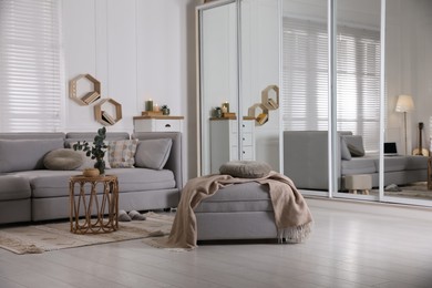 Comfortable grey sofa, ottoman and wardrobe with mirror doors in living room interior