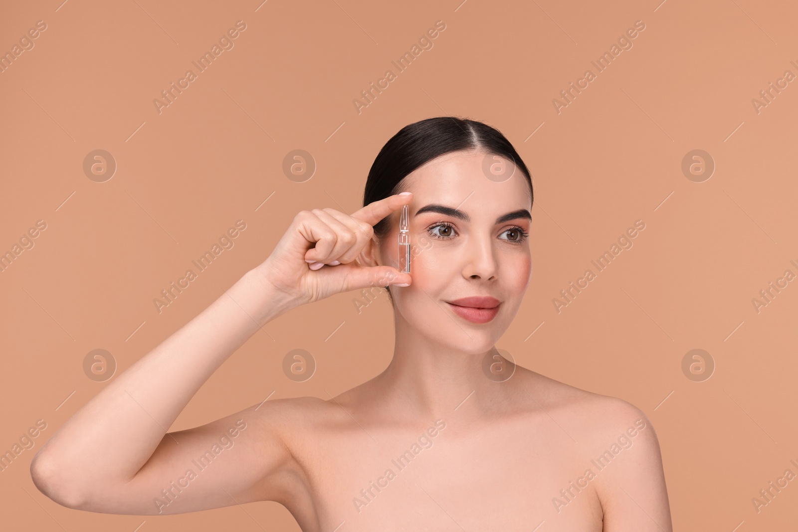 Photo of Beautiful young woman holding skincare ampoule on beige background