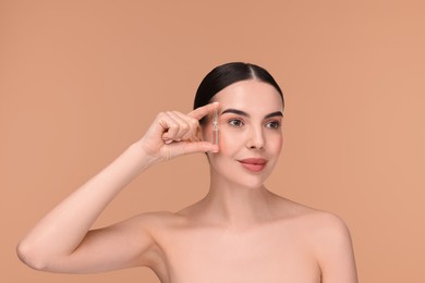 Beautiful young woman holding skincare ampoule on beige background