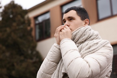 Photo of Sick young man coughing on city street. Cold symptoms