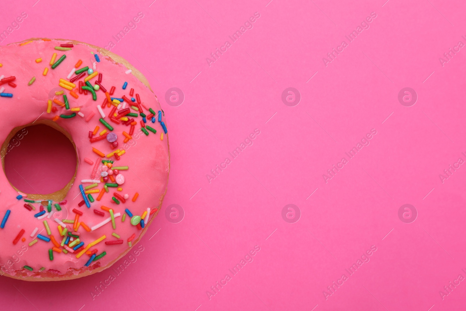 Photo of Sweet glazed donut decorated with sprinkles on pink background, top view and space for text. Tasty confectionery