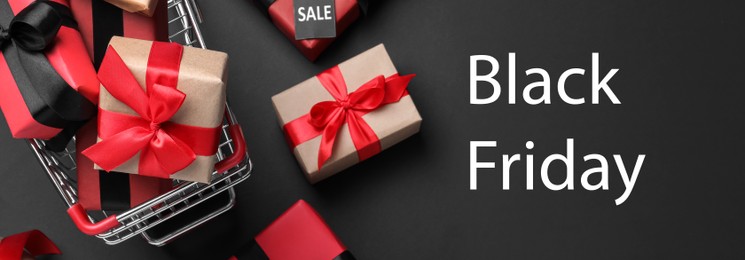 Image of Cart with gift boxes on dark background, flat lay. Black Friday sale