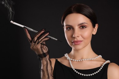 Woman using long cigarette holder for smoking on black background