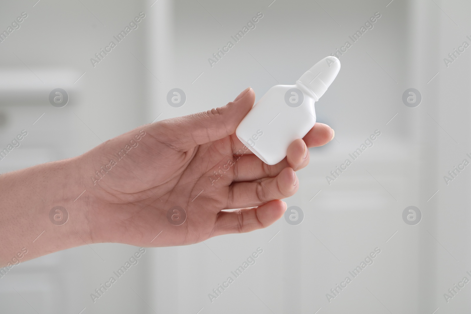 Photo of Woman holding nasal spray bottle indoors, closeup