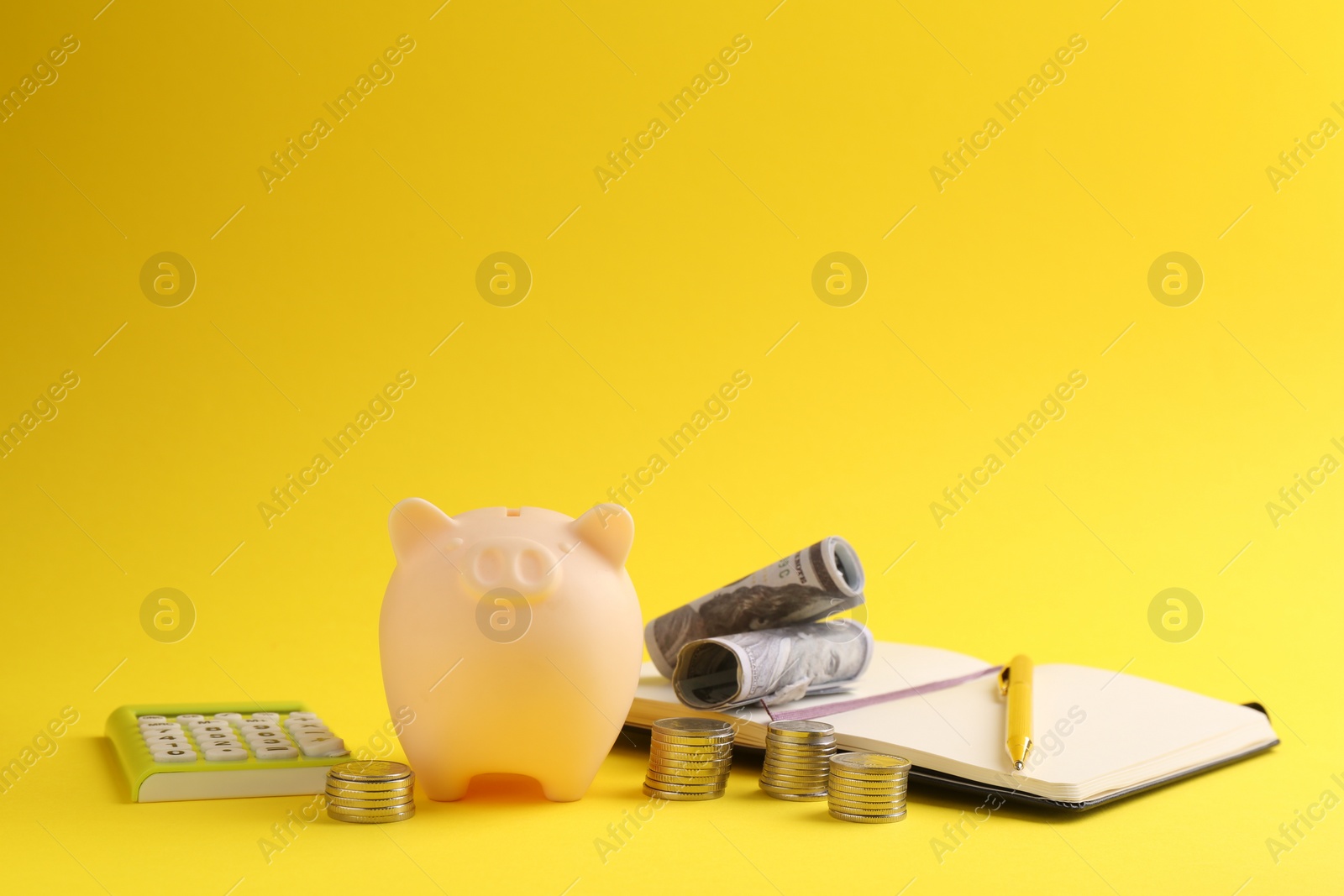 Photo of Financial savings. Piggy bank, money, calculator and stationery on yellow background
