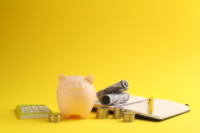 Photo of Financial savings. Piggy bank, money, calculator and stationery on yellow background