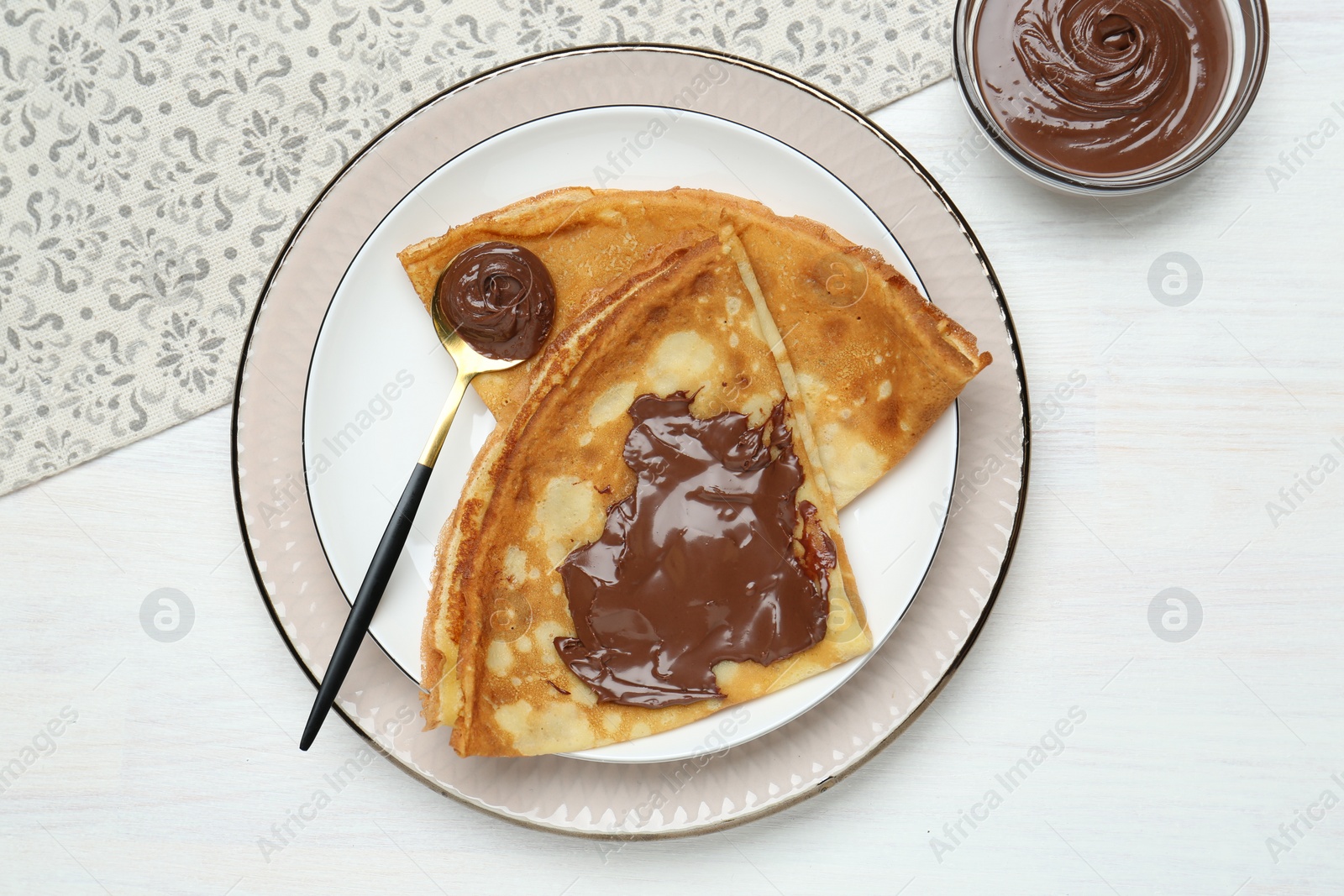 Photo of Tasty crepes with chocolate paste served on white wooden table, flat lay