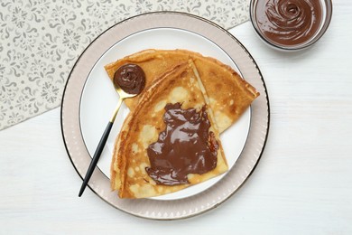 Tasty crepes with chocolate paste served on white wooden table, flat lay