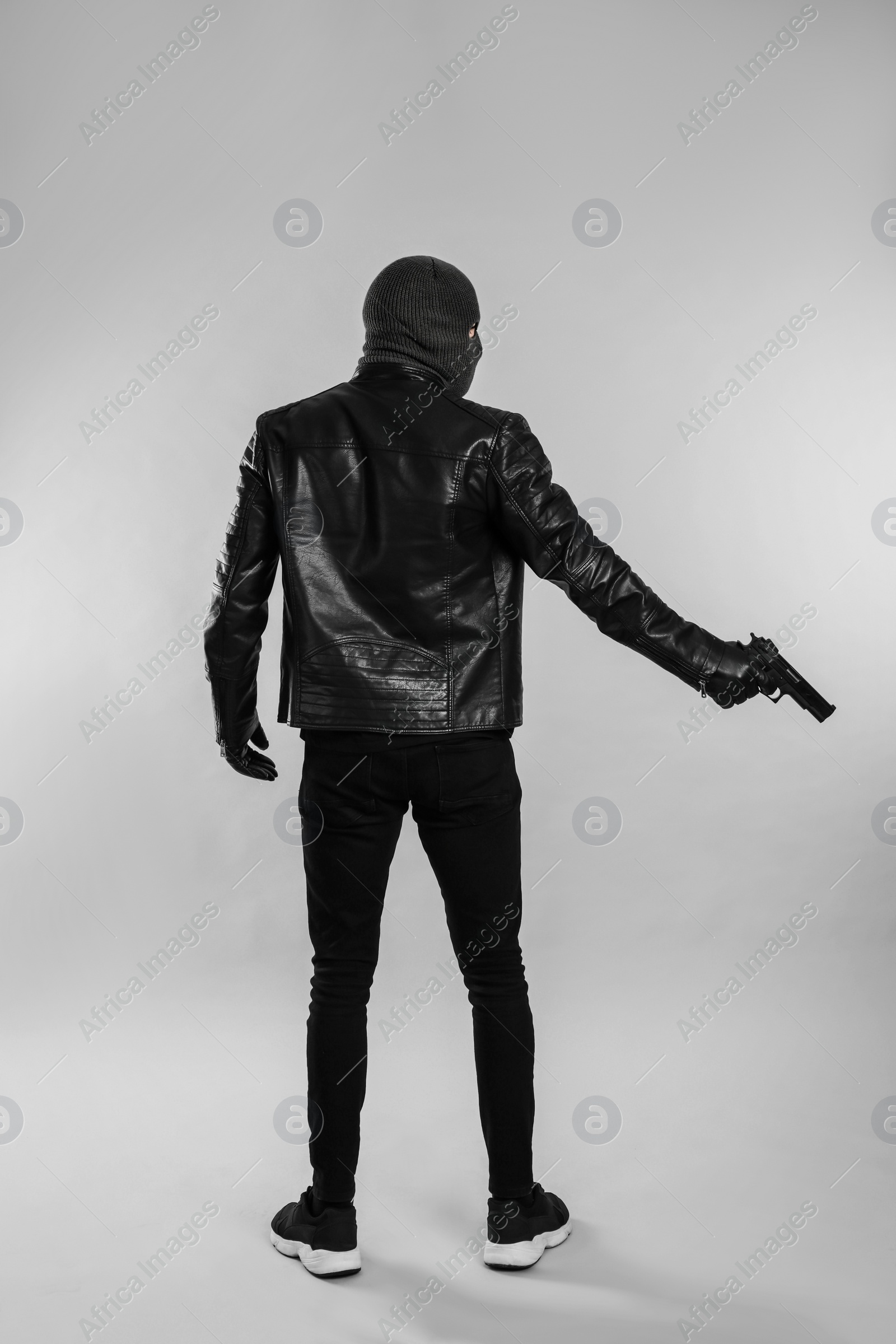Photo of Man wearing knitted balaclava with gun on light grey background, back view