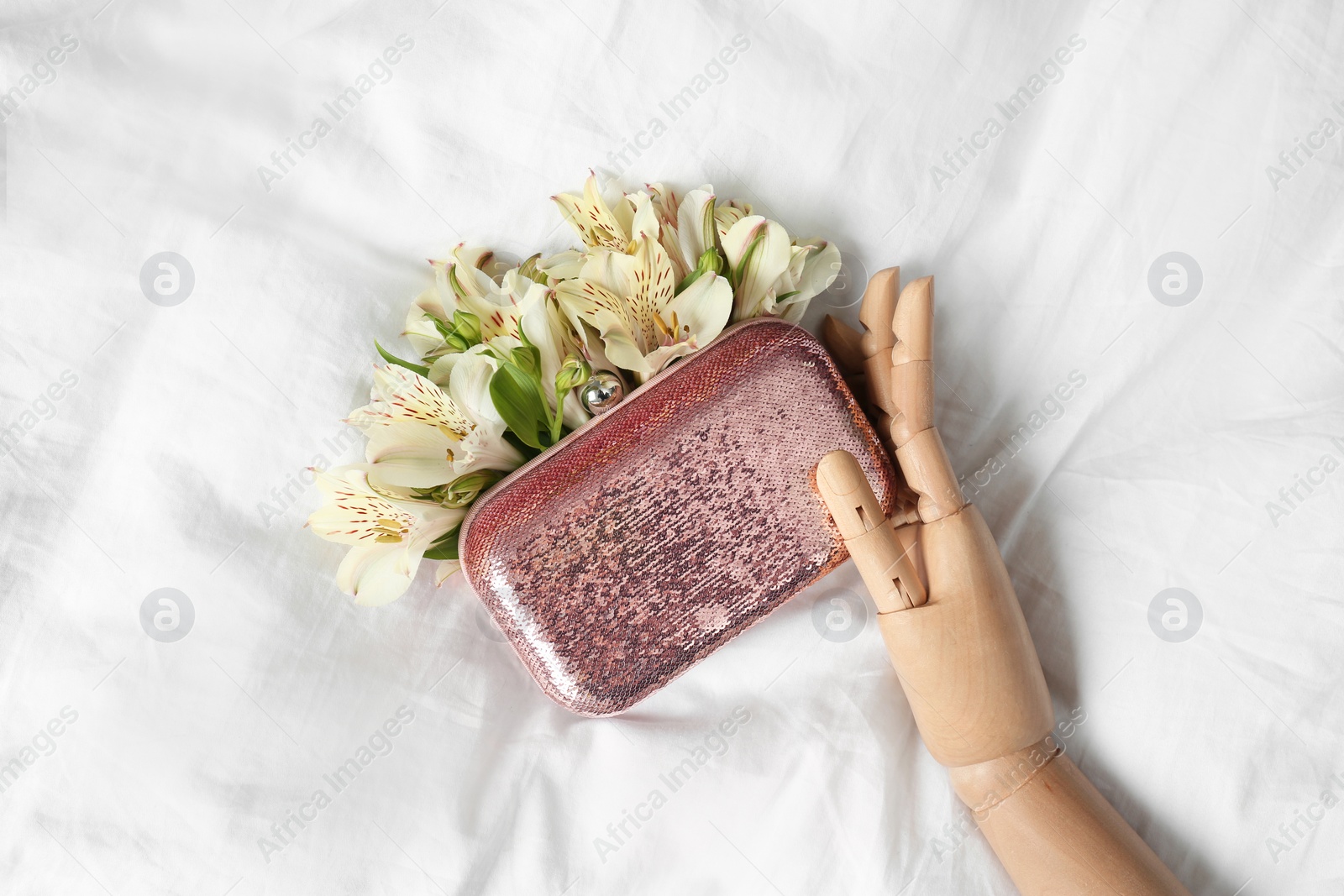 Photo of Stylish bag with spring flowers and wooden mannequin hand on crumpled sheet, flat lay