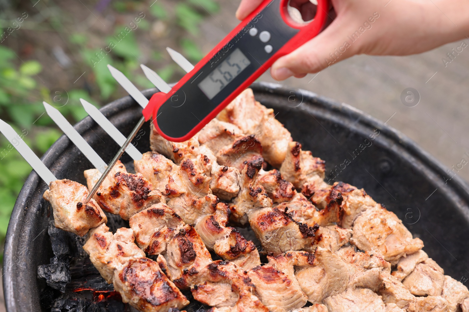 Photo of Man measuring temperature of delicious kebab on metal brazier outdoors, closeup