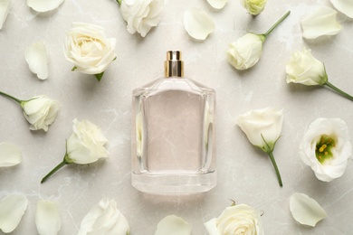 Flat lay composition of bottle with perfume and flowers on light grey marble background