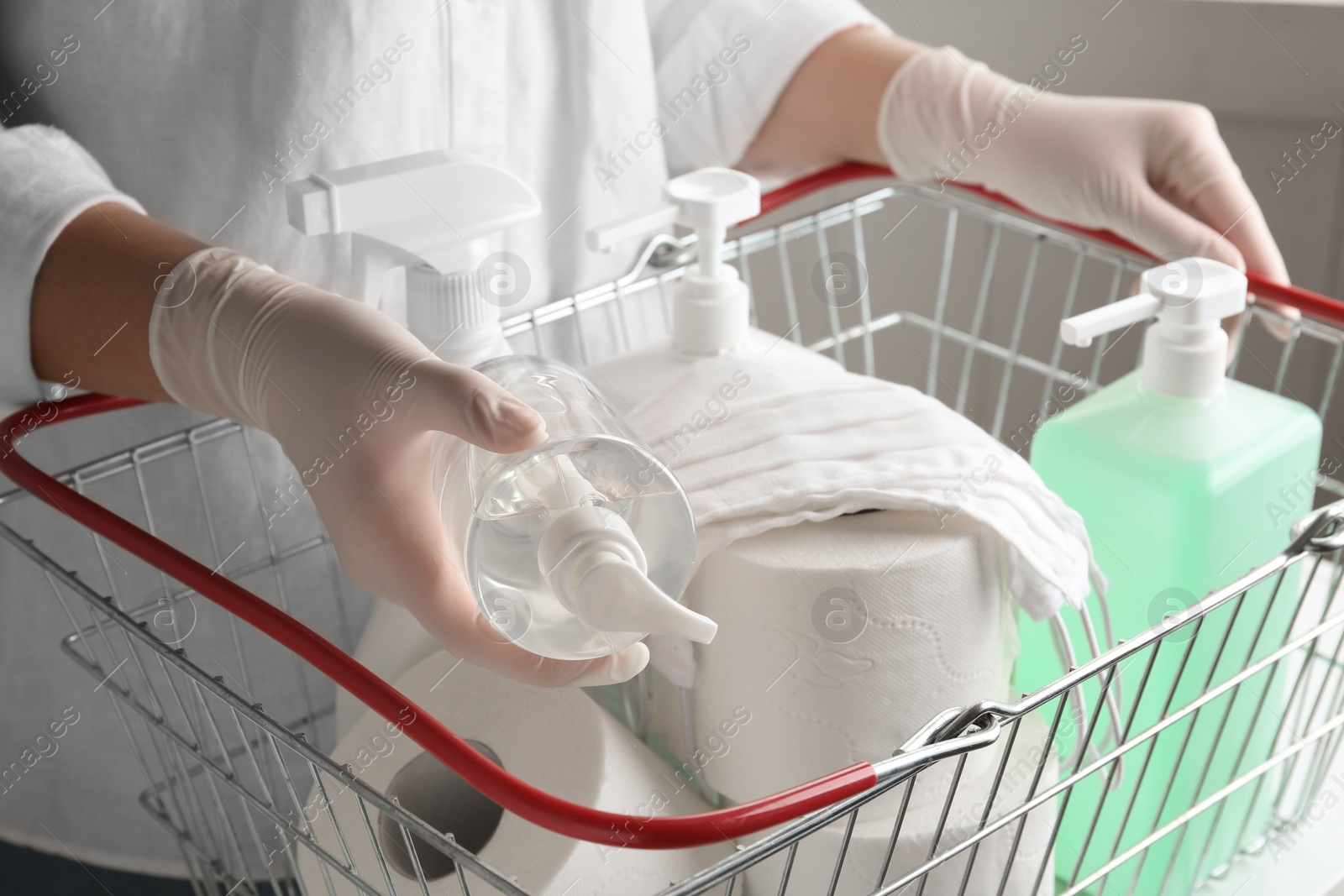 Photo of Woman with shopping basket full of antiseptics and toilet paper, closeup. Panic caused by virus