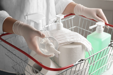 Photo of Woman with shopping basket full of antiseptics and toilet paper, closeup. Panic caused by virus