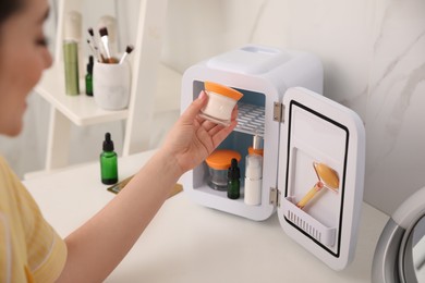 Woman taking cosmetic product out of mini refrigerator indoors, closeup