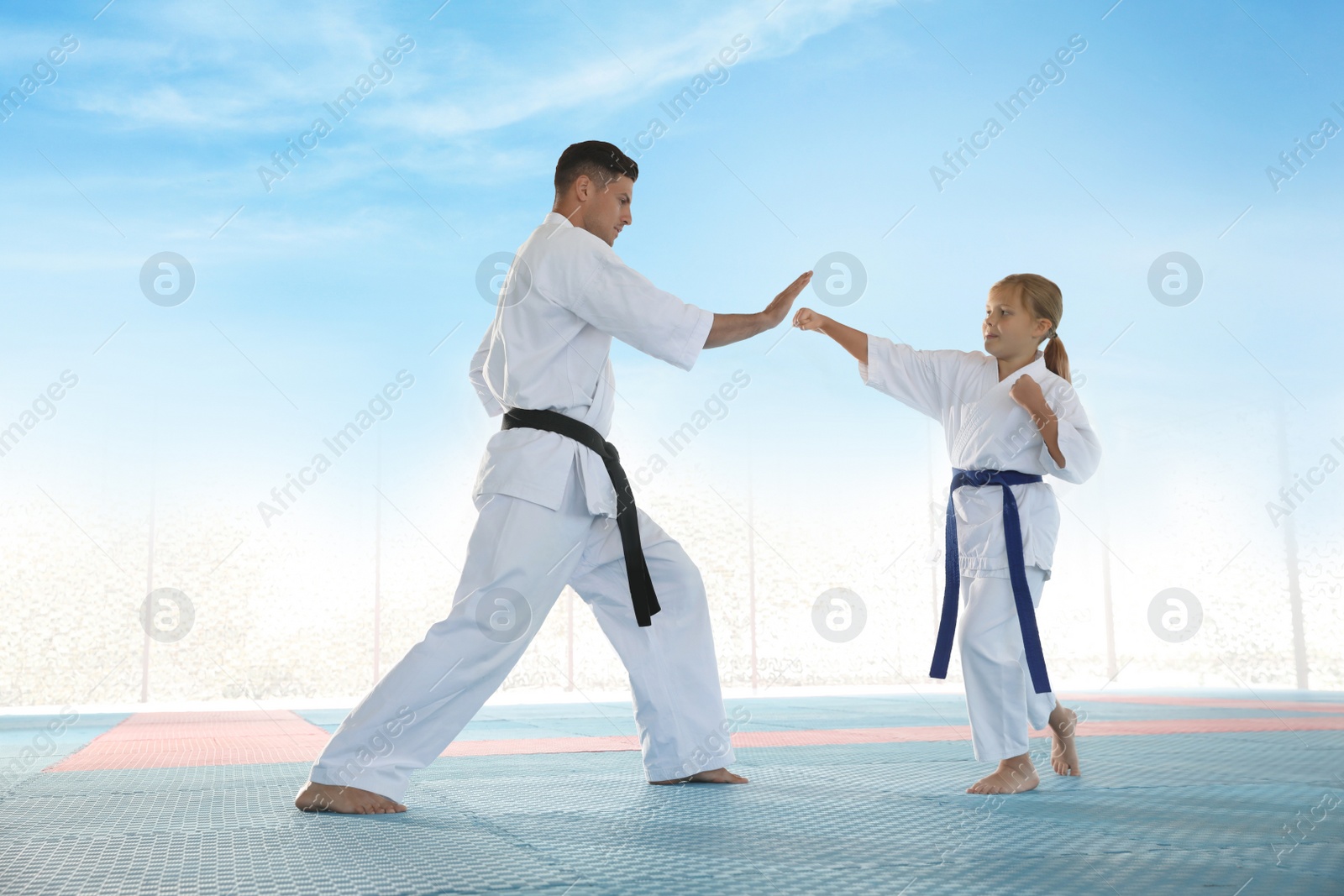 Photo of Girl practicing karate with coach on tatami outdoors