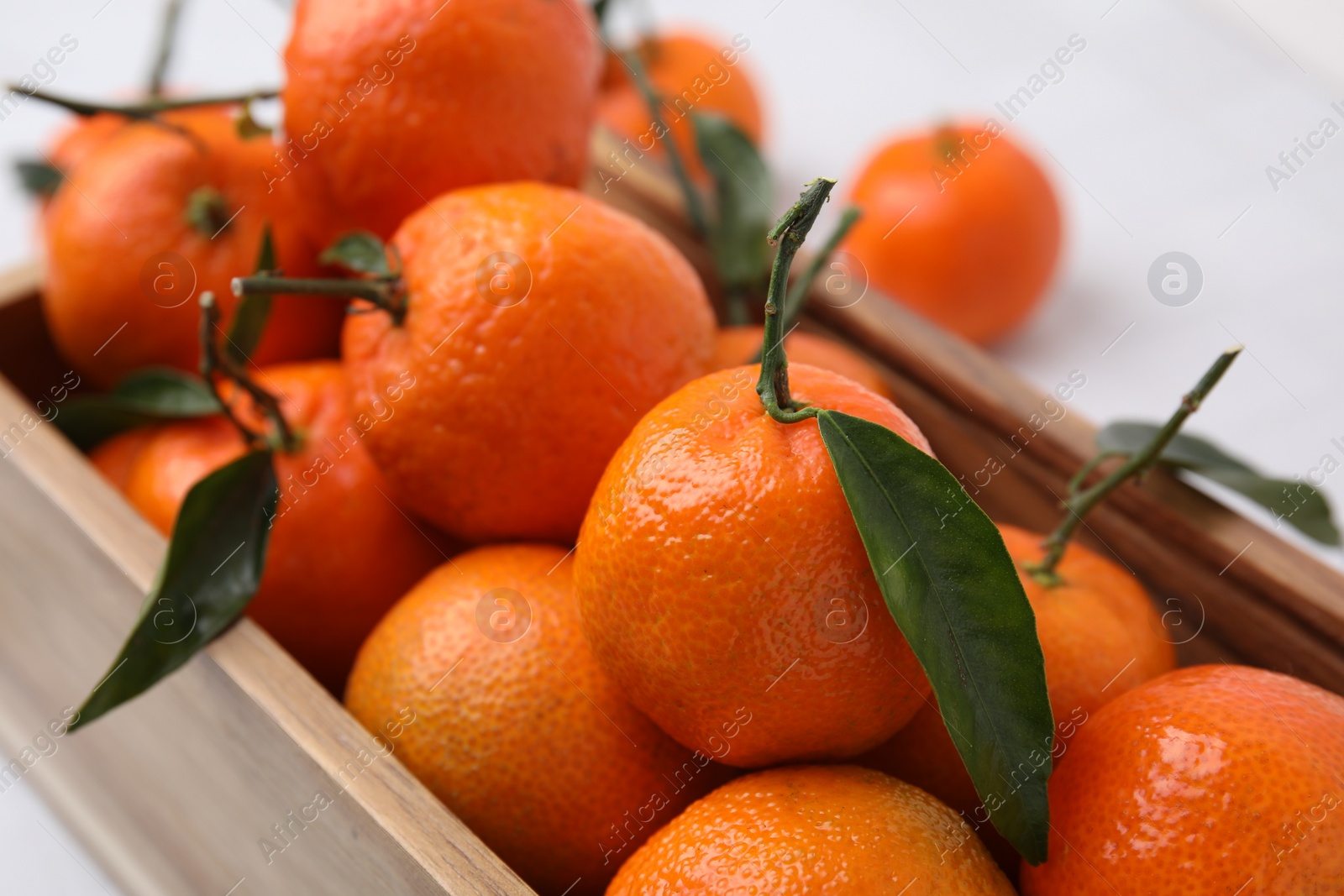 Photo of Wooden crate with fresh ripe tangerines and leaves on white table, closeup