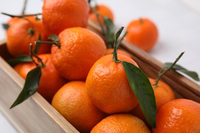 Wooden crate with fresh ripe tangerines and leaves on white table, closeup