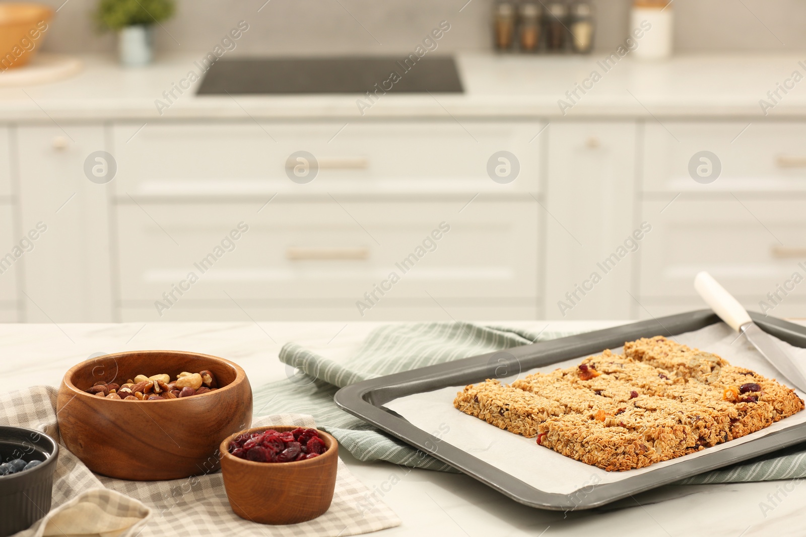 Photo of Baking tray with granola bars and ingredients on table in kitchen, space for text