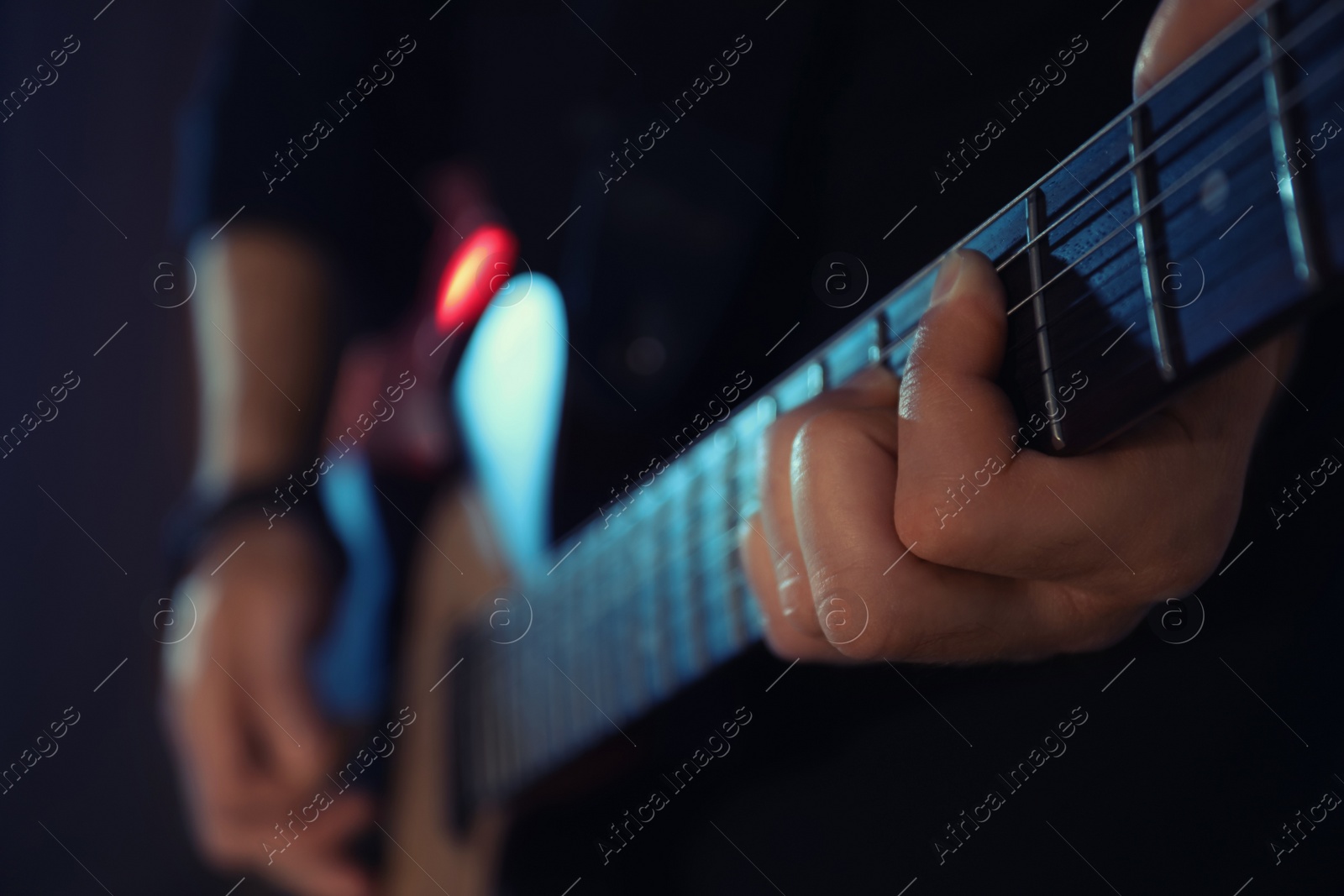 Photo of Man playing electric guitar on dark background, closeup. Rock music