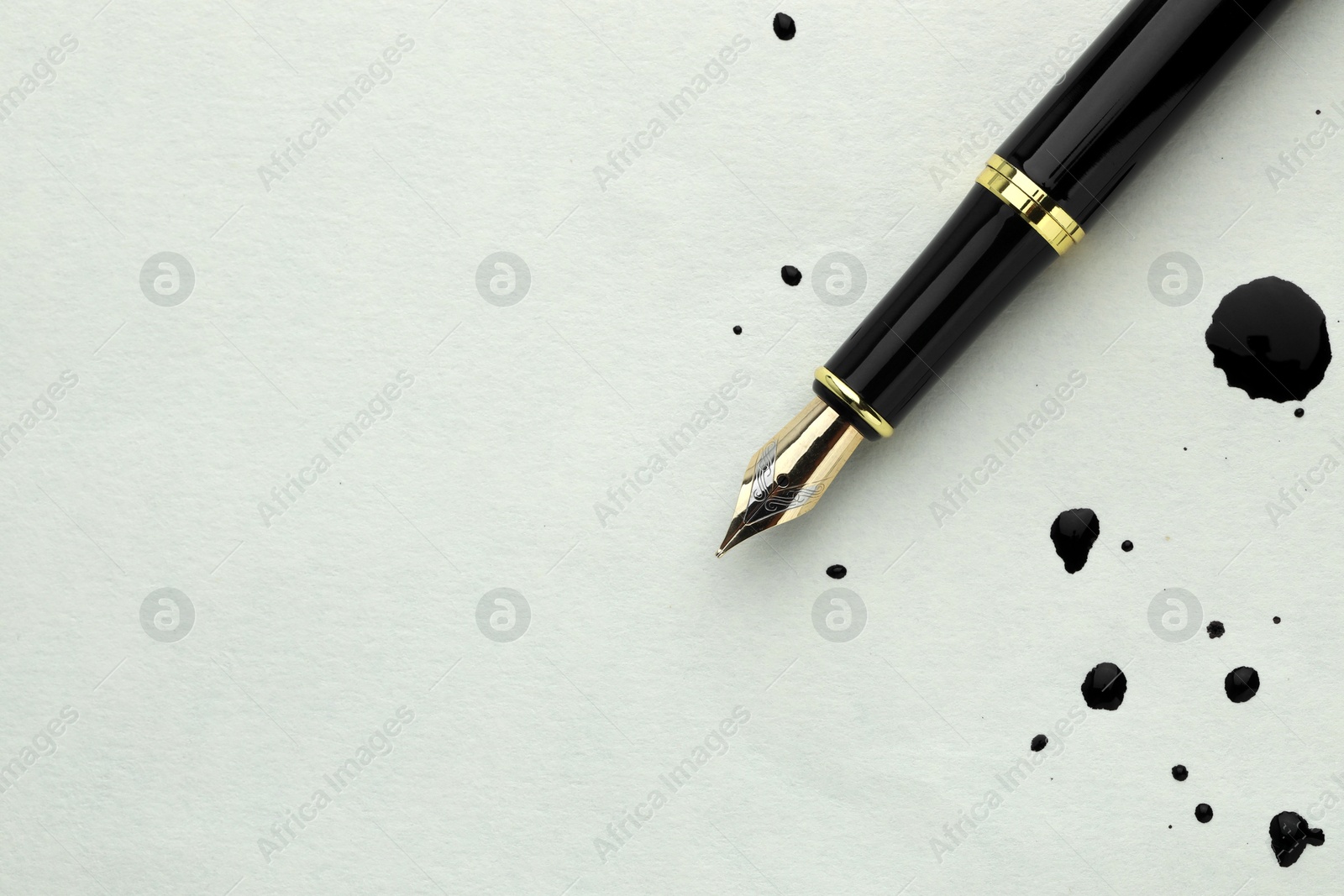 Photo of Stylish fountain pen on paper with drops of ink, top view. Space for text