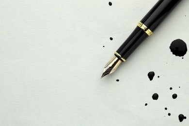 Stylish fountain pen on paper with drops of ink, top view. Space for text