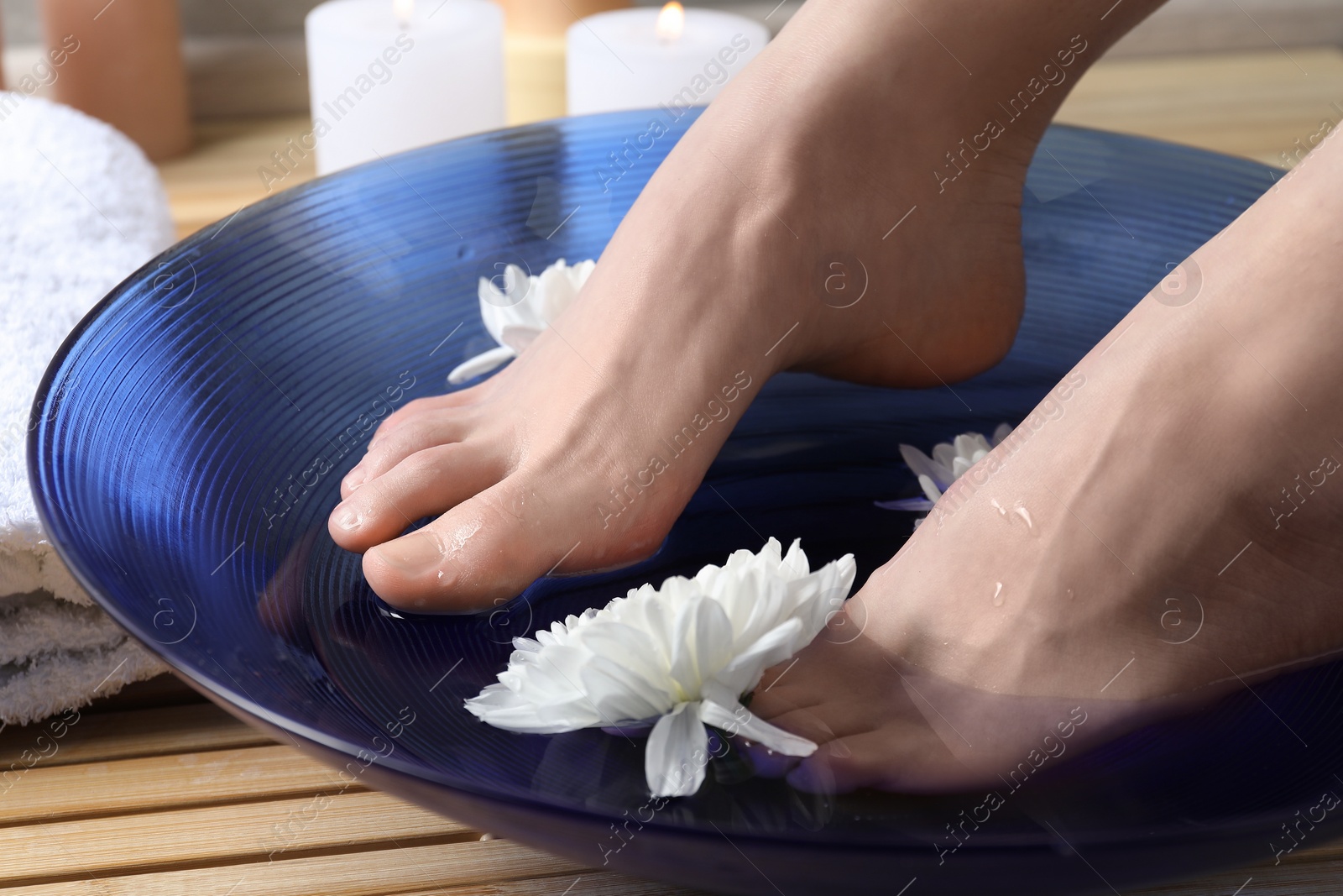 Photo of Woman soaking her feet in bowl with water and flowers on floor, closeup. Spa treatment